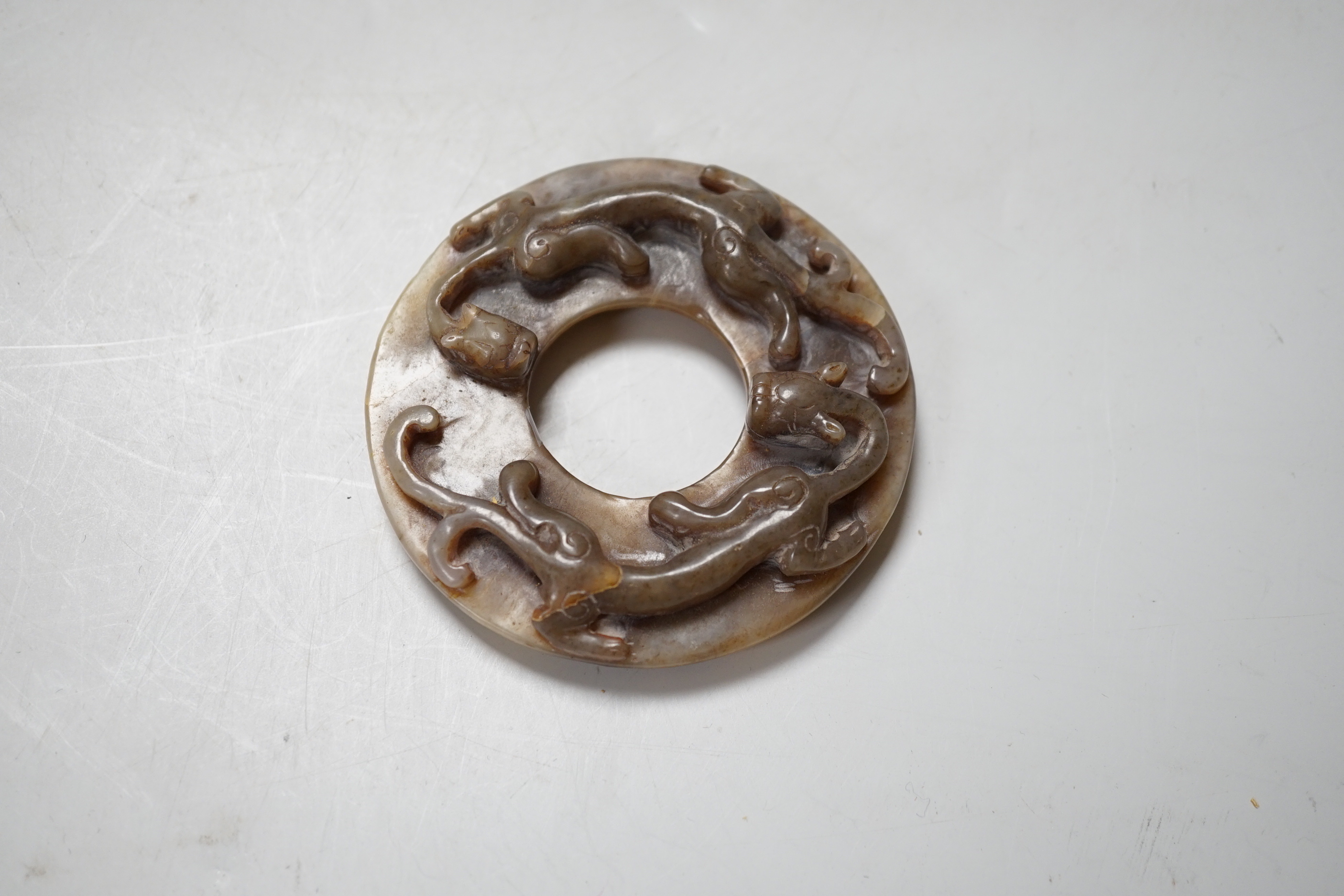 A Chinese brown and celadon jade ‘chilong’ bi disc, probably Ming dynasty, 8cm